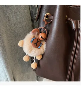 Detail of a khaki plush bag charm with leather accents on a brown leather handbag