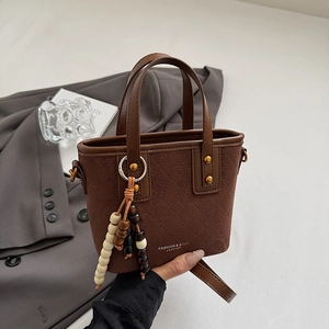 Détail d'un sac seau matelassé marron avec pompon en perles et bandoulière élégante