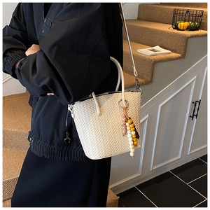 Close-up of white woven tote bag with colorful bead pendant in a lifestyle setting