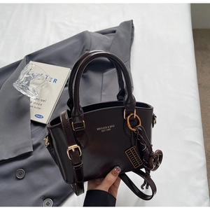 Detail of a dark brown leather handbag with gold metal hardware and a unique charm