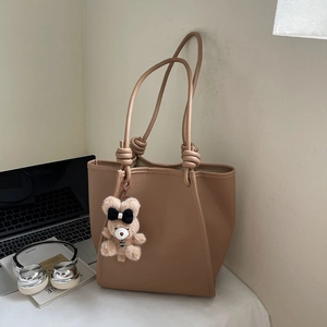 Brown leather tote bag with knot strap detail and bear charm in a desk setting