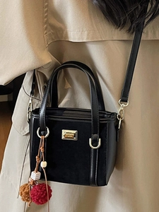 Fashionable black bucket bag with a plush charm pendant and gold metal logo plaque