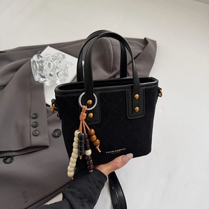 Détail du sac à main noir matelassé avec clous dorés et breloque en perles de bois sur veste