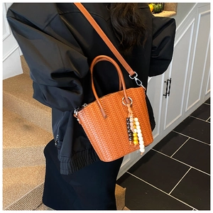 Close-up of woven caramel orange bucket bag with beaded charm and leather texture