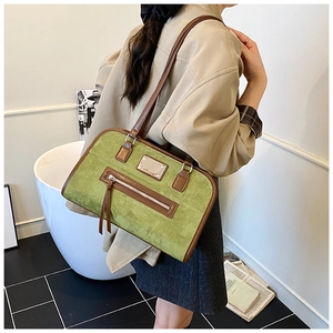 Detailed view of an olive green suede shoulder bag with brown leather trim and metal tag
