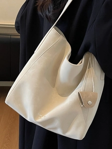 Grand sac cabas beige minimaliste avec pochette assortie, porté à l'épaule sur un manteau