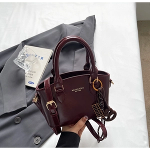 Close-up of wine red glossy handbag with gold metal hardware and detachable strap detail