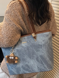 Large grey-blue textured tote bag with brown leather trim and a plush monster charm