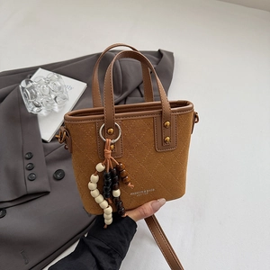 Détail du sac seau en cuir marron avec motifs matelassés et breloque perlée élégante