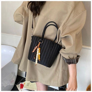 Detail of black woven bucket bag with beaded tassel charm and circular handles