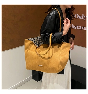 Detail of ginger yellow suede tote bag with reinforced straps and elegant branded metal plaque