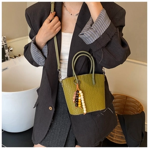 Detail of green woven bucket bag with colorful beaded handle and leather strap