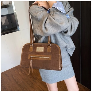 Detail of vintage brown suede shoulder bag with front zipper and metal logo plate