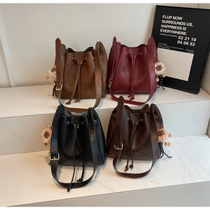 Close-up of stylish leather drawstring bucket bags with cute plush doll charms on display