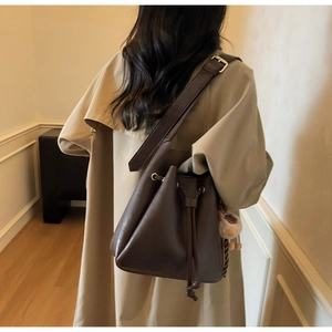 Detail view of brown leather bucket bag with plush charm on khaki trench coat