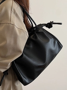 Minimalist black lychee textured leather drawstring bucket bag with knotted shoulder strap