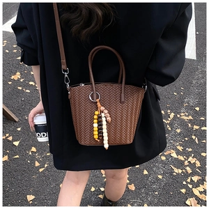 Detail view of brown woven texture handbag with beaded charm worn by a model