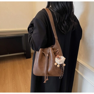 Brown leather bucket bag with drawstring and plush charm shown on model in minimalist room