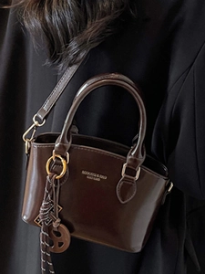 Brown faux leather crossbody bag with shiny finish and gold branding on black blazer background