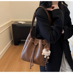 Detailed view of a vintage brown bucket bag with drawstring and white plush charm on a model