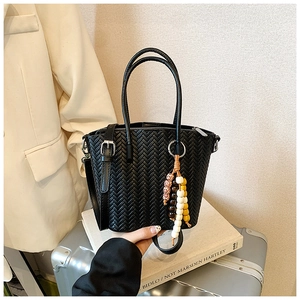 Detailed view of black woven crossbody bag with artistic multi-color beaded pendant