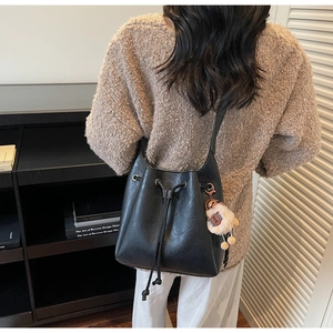 Detail of black drawstring bucket bag with leather texture and cute plush charm pendant