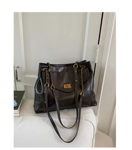 Macro detail of dark leather tote bag with vintage gold turn-lock closure and chain strap