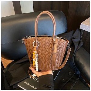 Detail of a brown woven bucket bag with a decorative bead charm and twin top handles