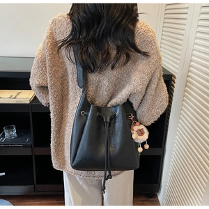 Detail of black PU leather bucket bag with drawstring closure and cute sheep pendant