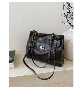 Close-up of black leather tote bag with gold chain strap and metal turn-lock on stone table