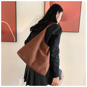 Detail of a brown suede tote bag featuring a minimalist triangular silhouette on a model