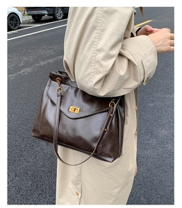 Close-up of a large dark brown leather tote bag with gold chain and twist-lock on a model