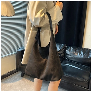 Detail view of large dark suede hobo tote bag worn by a model in a modern room
