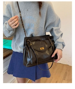 Detail of black faux leather tote bag featuring a gold twist lock and chain shoulder strap