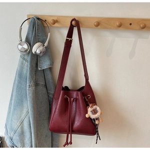 Detail of dark red leather bucket bag with lion plush pendant on a wooden hanger