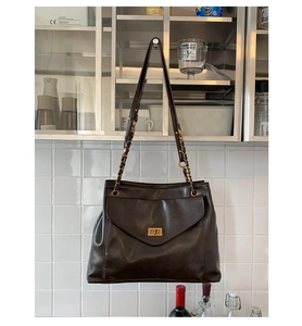 Detail of dark brown tote bag showing gold turn-lock closure and chain leather strap