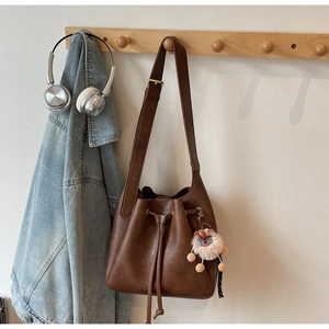 Close-up of brown leather drawstring bucket bag with a cute lion plush keychain