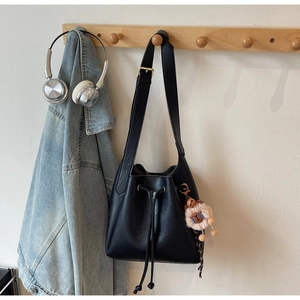 Detail of a black matte leather bucket bag with a lion plush charm on a wooden hook