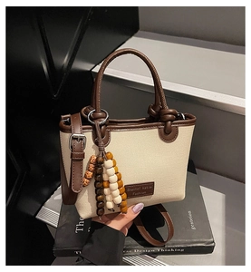 Detail of canvas tote bag with brown leather trim and colorful wooden bead charm