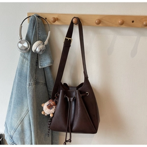 Detail view of brown leather bucket bag with drawstring and cute plush sheep pendant
