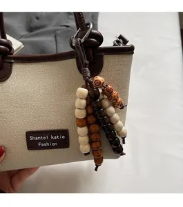 Detail of beige canvas bucket bag with brown leather trim and colorful wooden bead charms