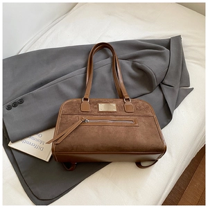 Détail d'un sac cabas vintage en daim marron avec une plaque dorée et une fermeture éclair