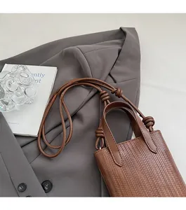 Detail of a brown woven mini bag featuring a sleek leather handle and a knotted rope strap