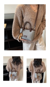 Detail of grey knitted bucket bag with brown leather straps and wooden bead charm