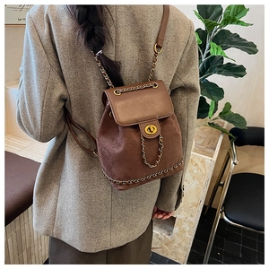 Close-up of vintage brown suede backpack with gold chain straps on a grey blazer