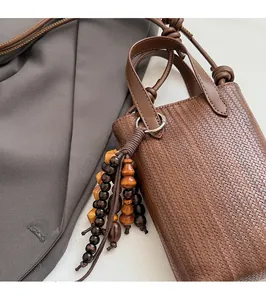 Detail of a brown woven mini crossbody bag featuring multi-colored wooden bead tassels