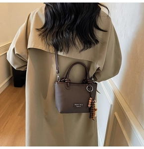 Detail of dark brown leather bucket bag with bead tassel on model in trench coat