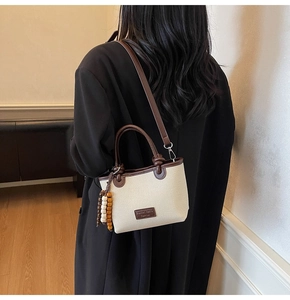 Detail view of canvas bucket bag with brown leather trim and decorative wooden beads
