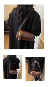Détail d'un sac cylindrique marron foncé vintage avec charms ethniques et bandoulière fine