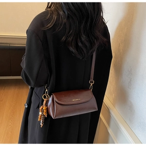Détail du sac bandoulière en cuir marron chocolat avec pompon en perles de bois et logo